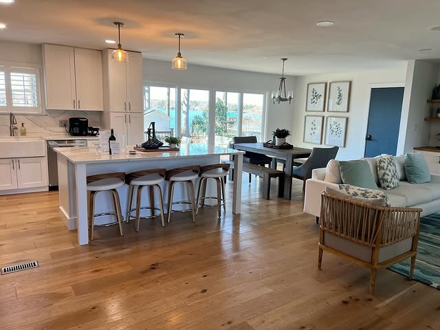 Spotlessly clean open-concept kitchen and living area with white cabinetry, hardwood floors, kitchen island with bar stools, dining table, and comfortable seating - showcasing our detailed home cleaning services in Charlotte