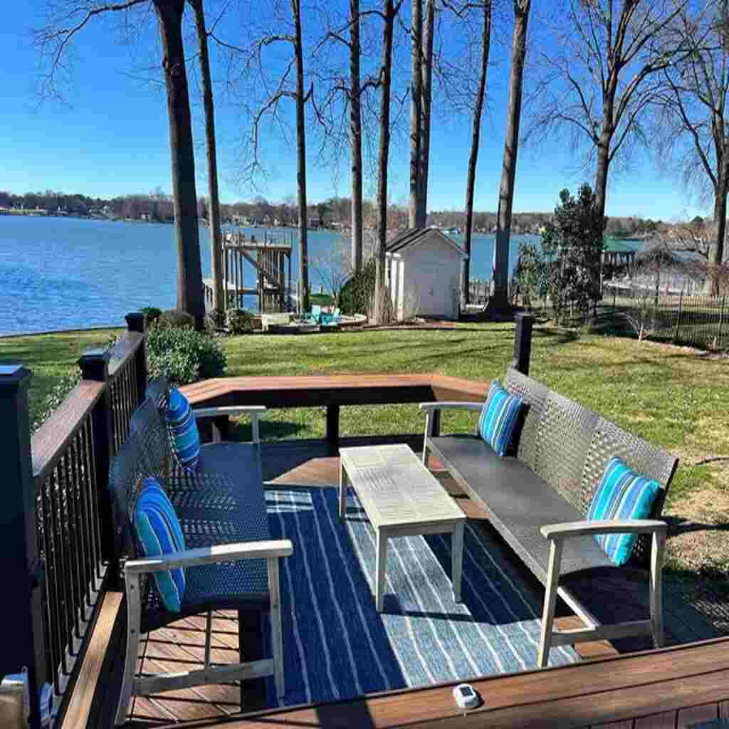 Pristine lakefront deck with outdoor furniture, blue accent pillows and rug, overlooking well-maintained lawn, lake, dock and boathouse - showcasing our specialized exterior cleaning services for Raleigh waterfront properties
