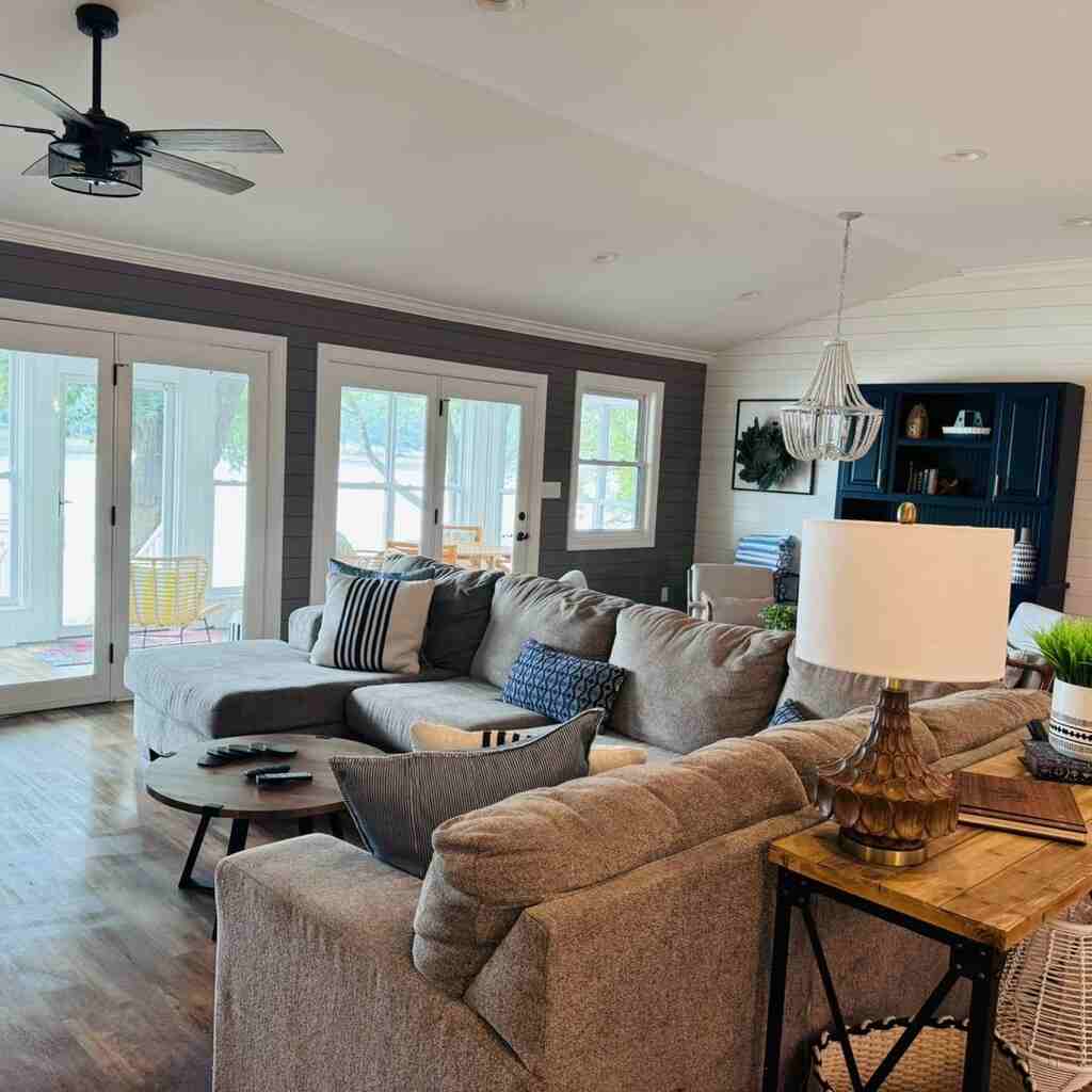 Beautifully cleaned modern living room with sectional sofa, hardwood floors, French doors, ceiling fan, elegant chandelier, accent walls, and tasteful décor - showcasing our premium residential cleaning services for Charlotte homes